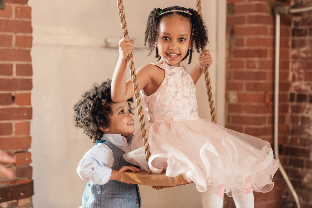 Young boy pushing his sister on a swing in the garden
