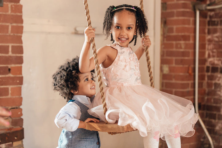 Young boy pushing his sister on a swing in the garden