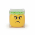 Moody squeeze face toy with yellow body and green fluffy hair in clear packaging on white background